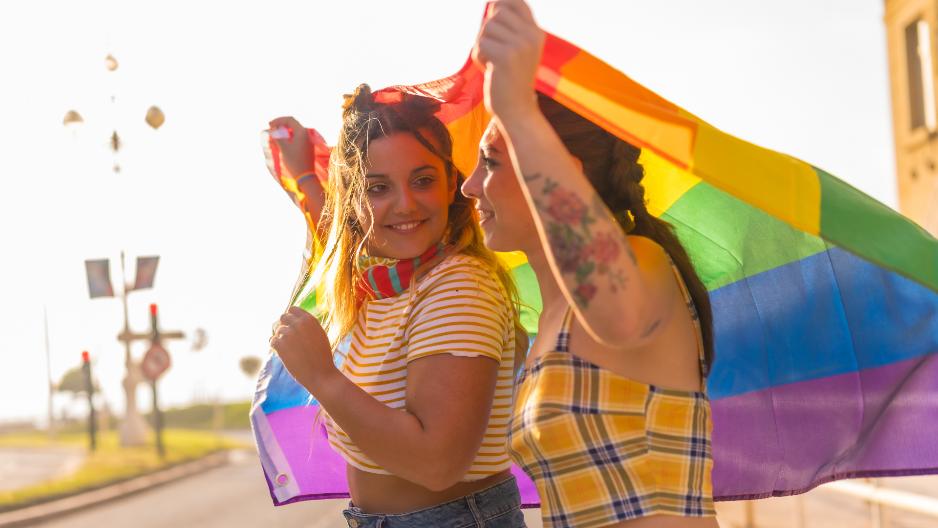 Zwei Menschen halten gemeinsam eine Regenbogenflagge über sich und lächeln sich an – Symbol für Liebe, Freiheit und Stolz innerhalb der LGBTQ+-Community.